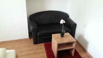 Un salon avec un canapé en cuir noir, une table d’appoint en bois sur laquelle est posée une orchidée blanche en pot, et un tapis rouge.