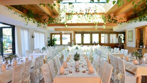 A long dining table set for a formal event with white tablecloths, chairs, and floral centerpieces. - Wirtshaus Nattererboden (Natters)