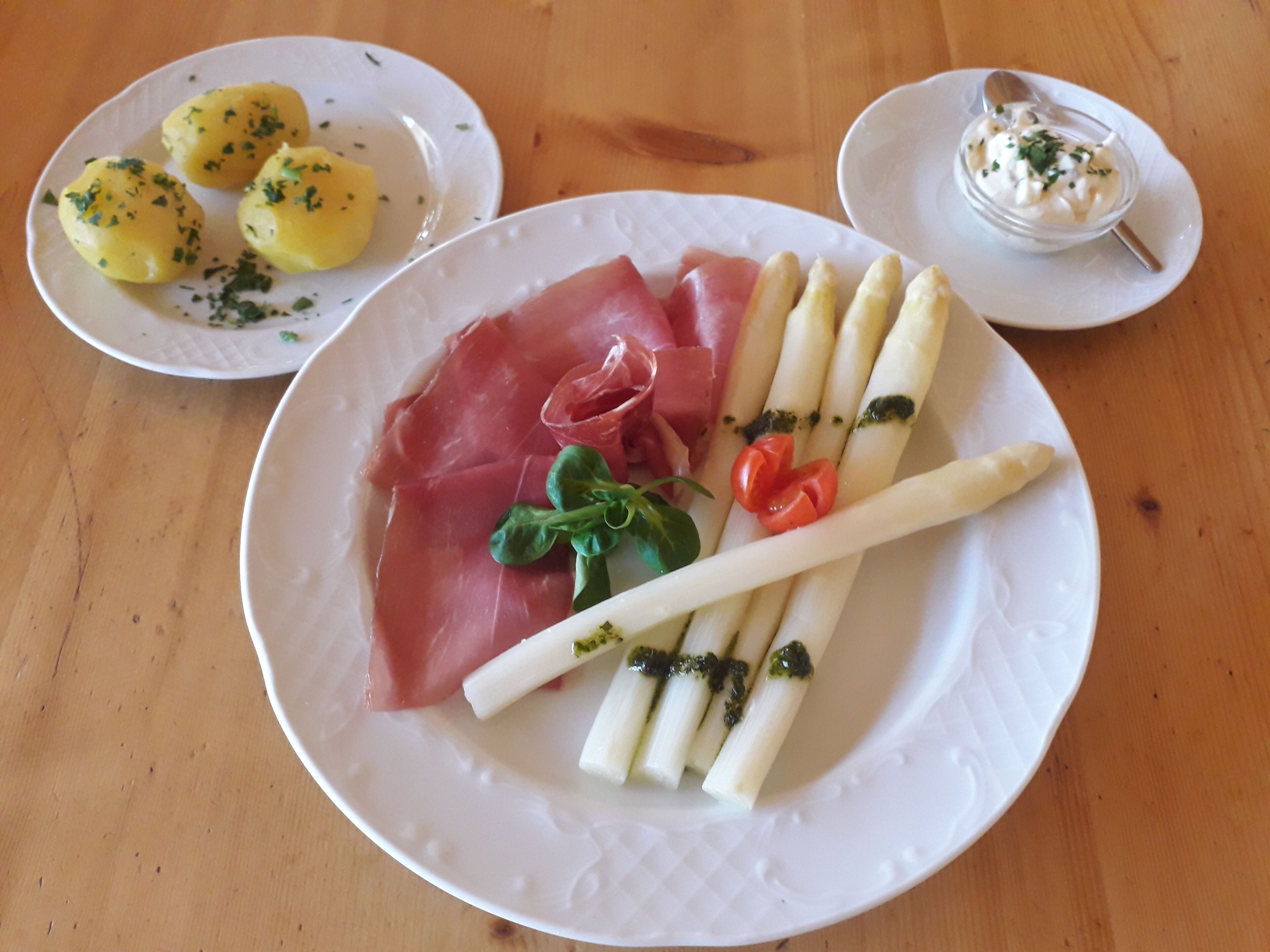 A plate with prosciutto, asparagus, cherry tomatoes, and a sprig of parsley.