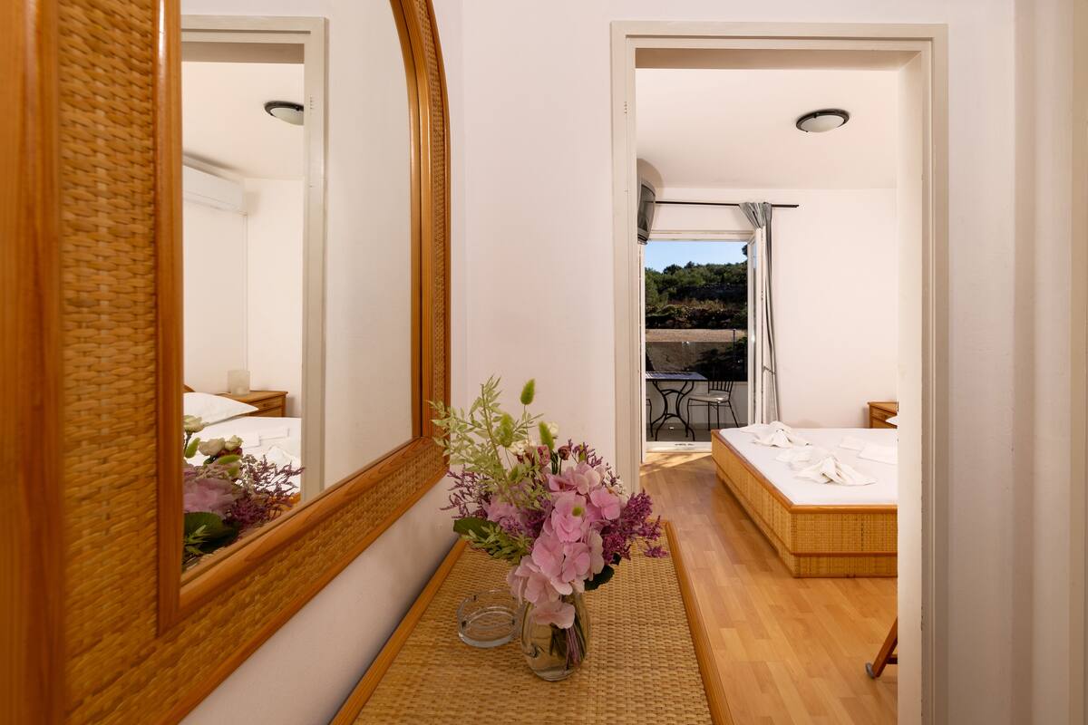 A bedroom with a bed, a bedside table, a mirror, and a vase with flowers.