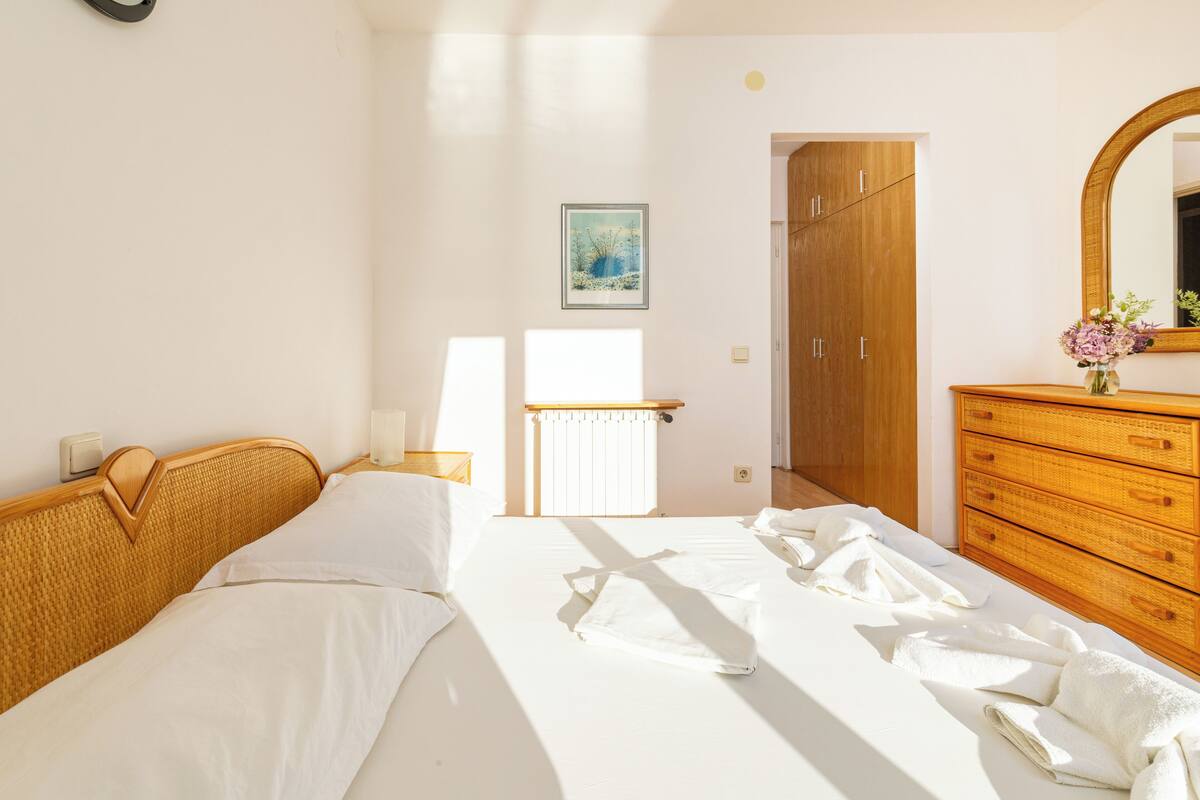 A hotel room with a bed, a wooden dresser, a mirror, and a radiator.