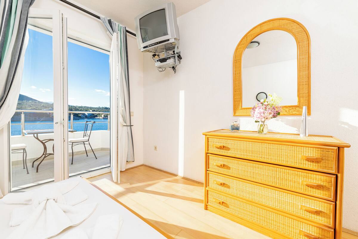 A hotel room with a balcony, a television mounted on the wall, a wicker dresser, and a mirror.
