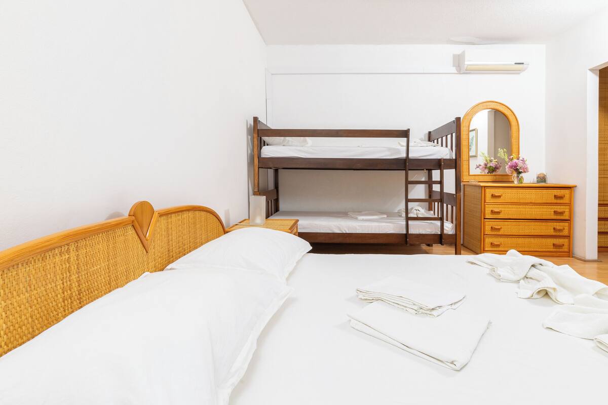 A bunk bed with a wooden headboard, a wooden dresser with drawers, and a mirror with a floral vase.
