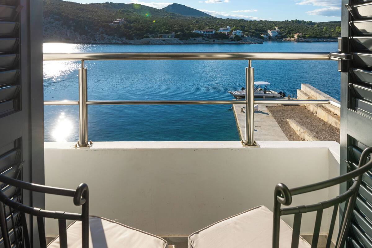 A balcony with a view of a lake, a table, and two chairs.