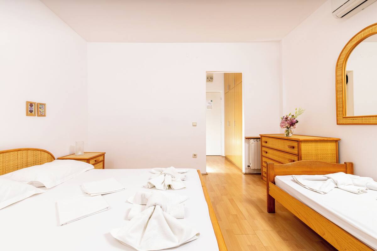 A hotel room with a large bed, a wooden dresser, a mirror, and a door leading to another room.