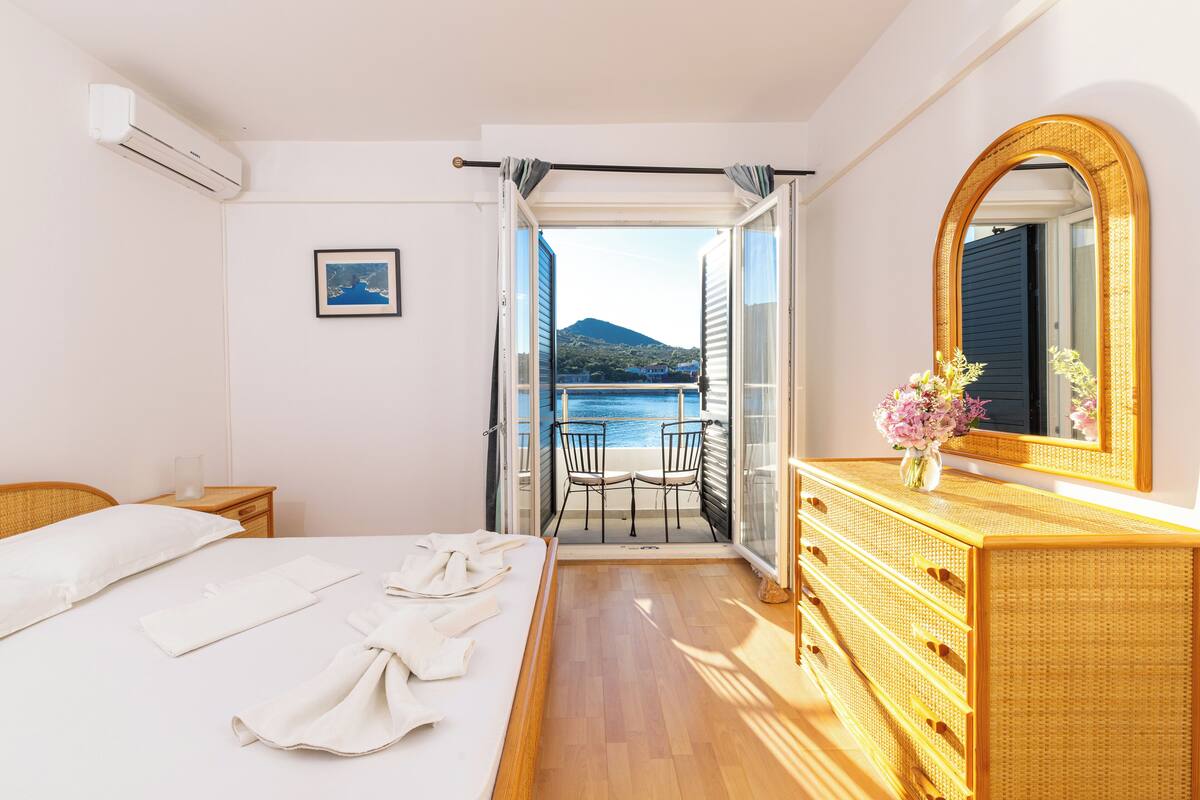 A hotel room with a bed, a dresser, a mirror, and a balcony with a view of the sea.