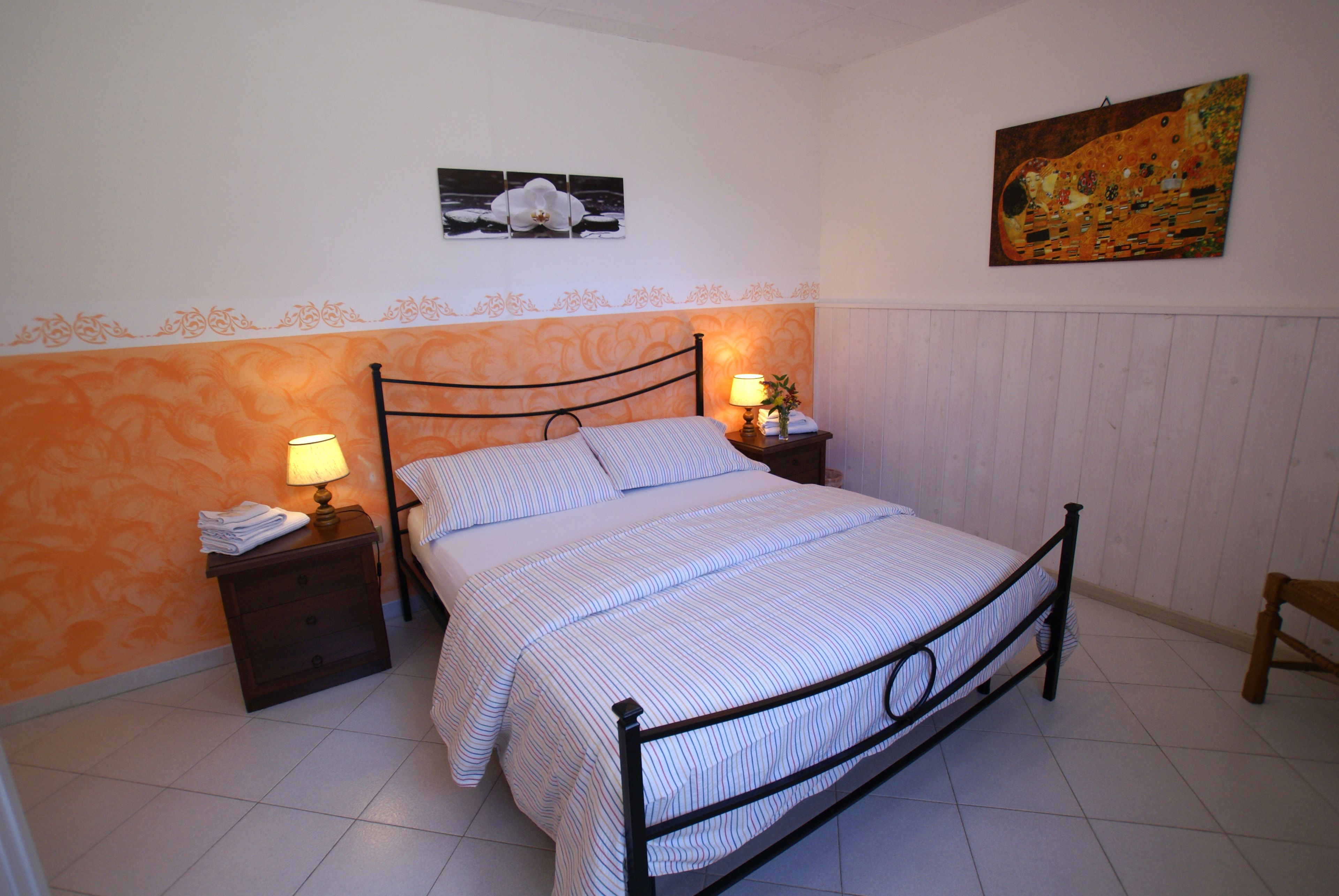 Un dormitorio con una cama, dos mesitas de noche con lámparas, una silla y obras de arte en las paredes.