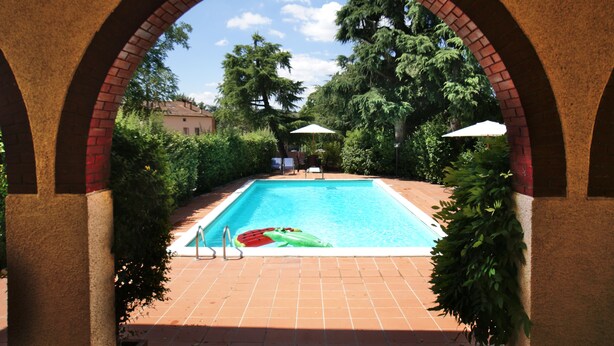 A swimming pool with a clear view through an arched brick structure, surrounded by lush greenery and a clear sky. - Il Querceto - B&B e Appartamenti Vacanze (Perugia)