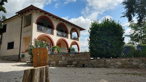 A two-story building with a stone wall in front, arched balconies, and a gravel driveway. - Il Querceto - B&B e Appartamenti Vacanze (Perugia)