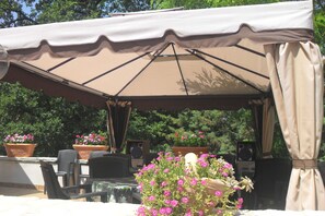 Une terrasse extérieure dotée d’un espace salon couvert, de plantes en pot et d’une table avec des chaises.