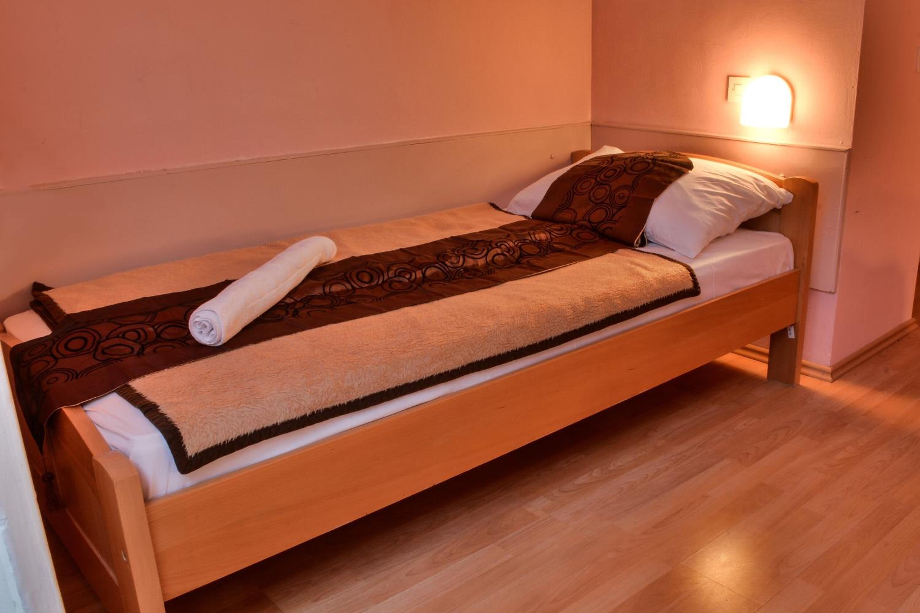 A single bed with a wooden frame, a patterned blanket, and a rolled towel.