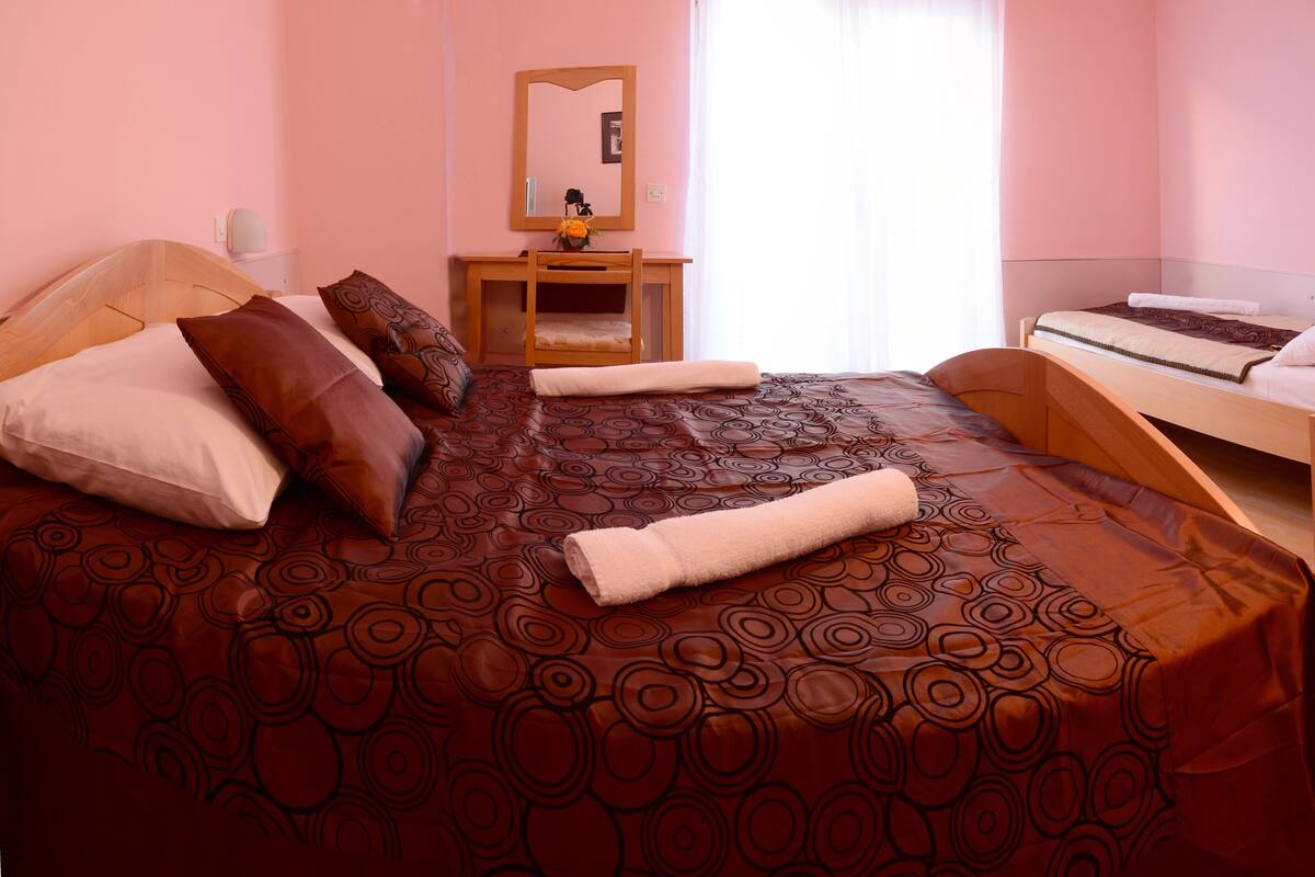 A bedroom with a large bed, a wooden bedside table, a mirror, and a small desk with a chair.
