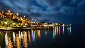 A waterfront scene with illuminated buildings and a calm body of water reflecting lights. - Hotel Art (Senj)