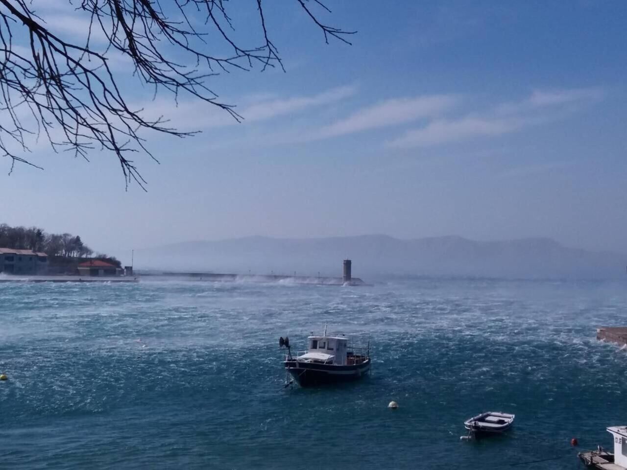 Un paysage côtier avec un phare à l’horizon, un petit bateau au premier plan et une mer calme.
