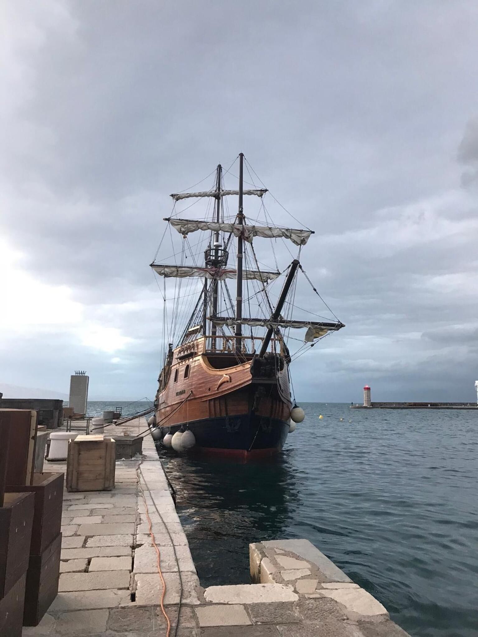 Un grand navire en bois était amarré à un quai, et une promenade en pierre menait à l’eau.