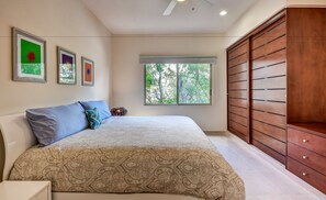 Un dormitorio con cama, armario, ventana con vista a árboles y cuadros en la pared.