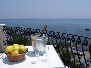 A table with a bucket of ice, a bottle of champagne, and a basket of apples on a balcony overlooking the sea. - Hotel Kalos (Giardini Naxos)