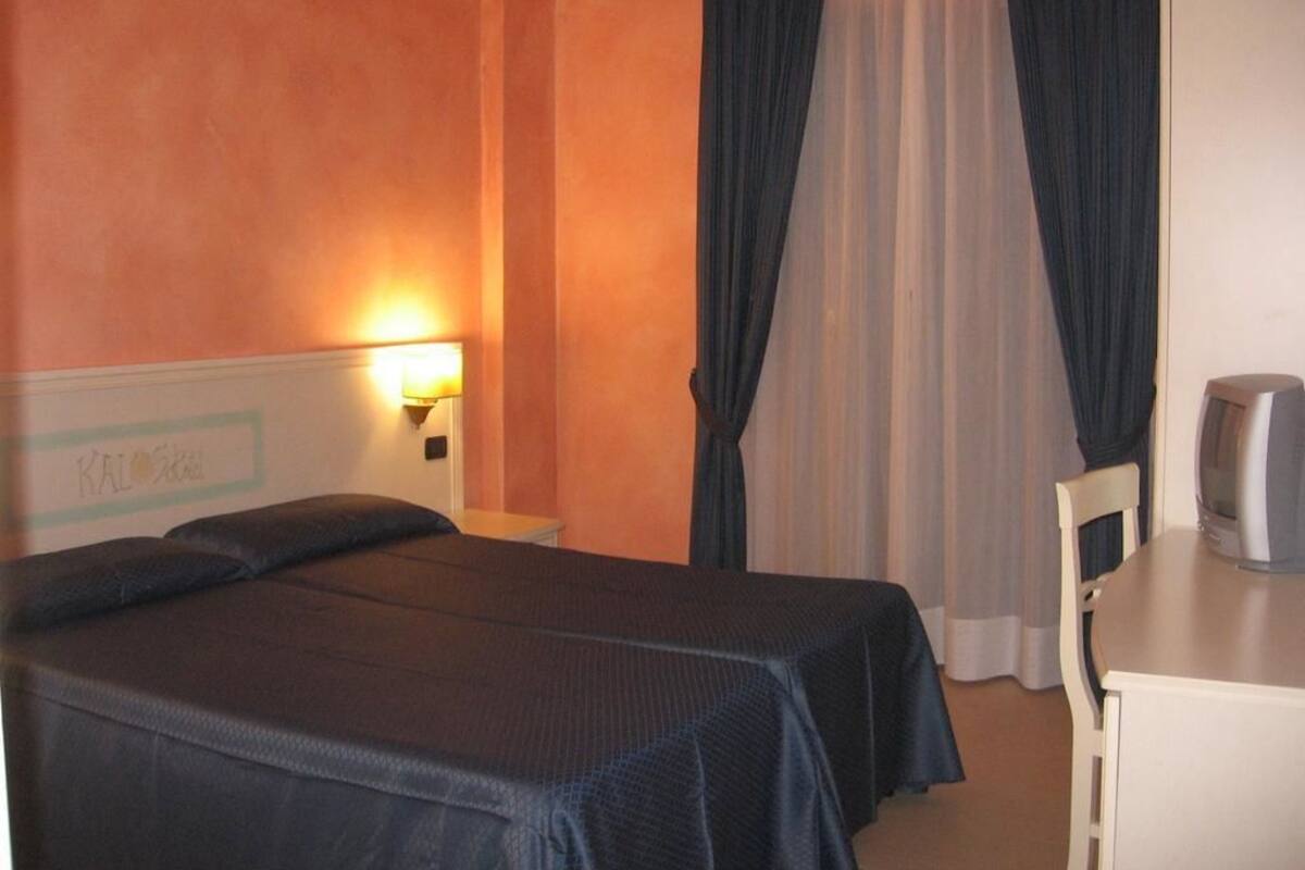 A hotel room with two beds, a desk, a television, and a wall-mounted lamp.