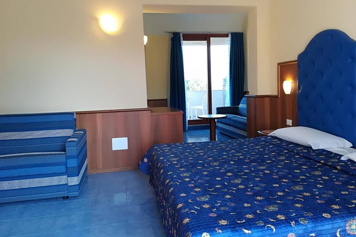 A hotel room with a bed, a sofa, a desk, and a view of the outside.