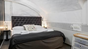Un dormitorio con cabecera capitonada, ropa de cama blanca y una mesita de noche con lámpara.