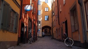 A narrow cobblestone street flanked by buildings with large windows and a clear blue sky above. - Hotell Skeppsbron (Stockholm)
