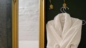 Un espejo con un marco dorado ornamentado, una bata blanca colgada de un gancho, y una cama con una colcha oscura al fondo.