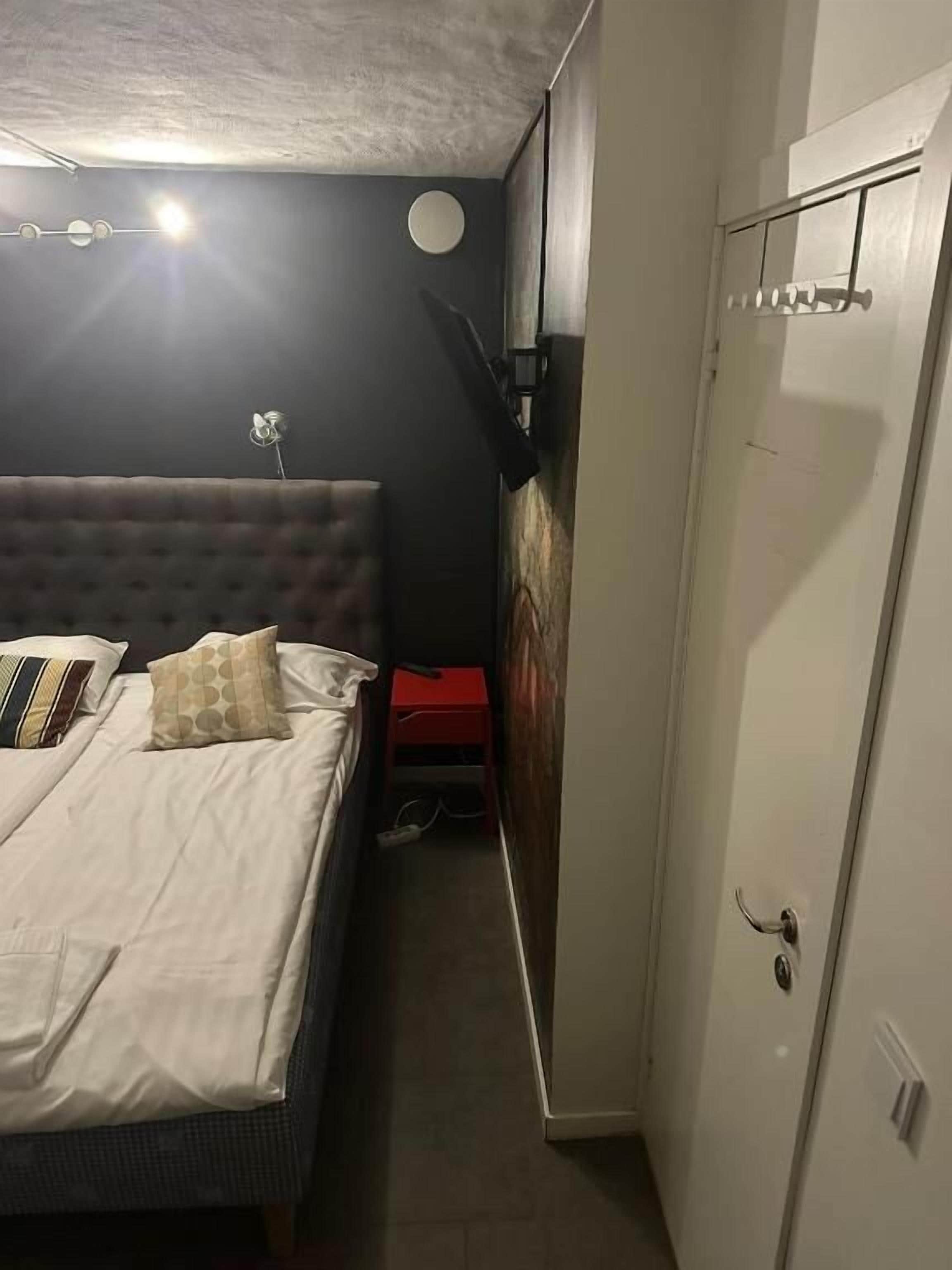 A bedroom with a bed, a wardrobe, a red cabinet, and a wall-mounted light fixture.