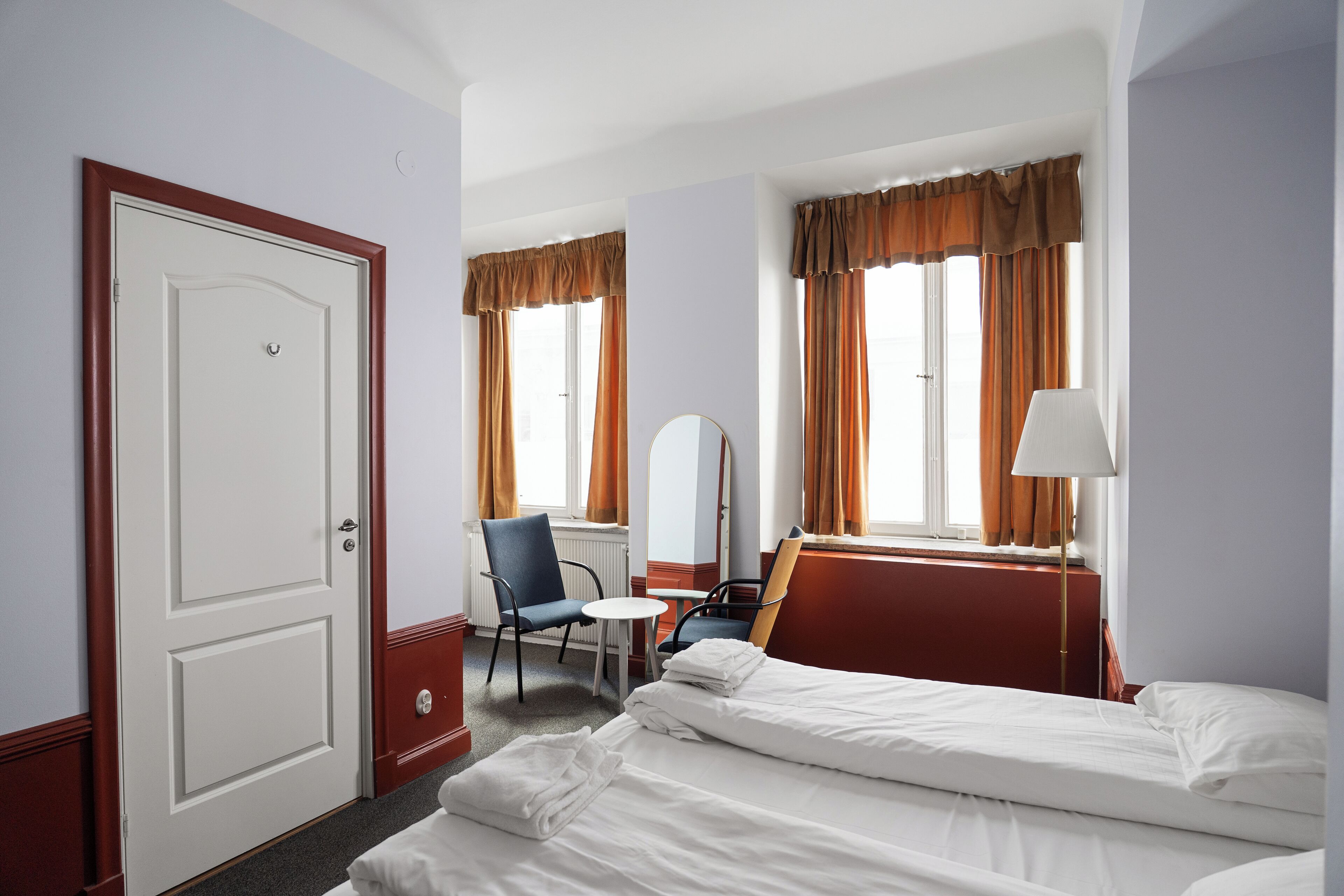 Et hotelværelse med seng, to stole, et lille bord, et spejl og en lampe.