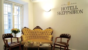 A room with a tufted sofa, two wooden chairs, a glass coffee table, and a wall sign reading "HOTEL SKEPPSBRON". - Hotell Skeppsbron (Stockholm)