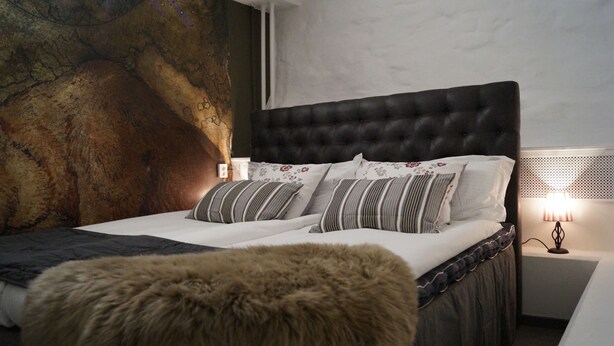 A bedroom with a tufted headboard, a large fluffy rug, and a nightstand with a lamp. - Hotell Skeppsbron (Stockholm)