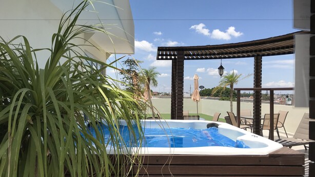A hot tub with a wooden deck, surrounded by potted plants, and overlooking a cityscape. - My Home Suites (Celaya)