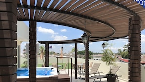 A covered outdoor area with a hot tub, lounge chairs, and a view of the city. - My Home Suites (Celaya)