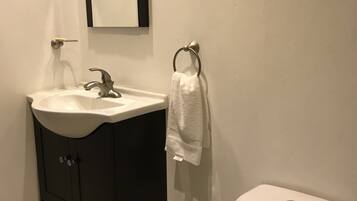 Une salle de bain avec un lavabo blanc, un meuble sombre, des toilettes et une serviette suspendue à un porte-serviette en forme d’anneau.