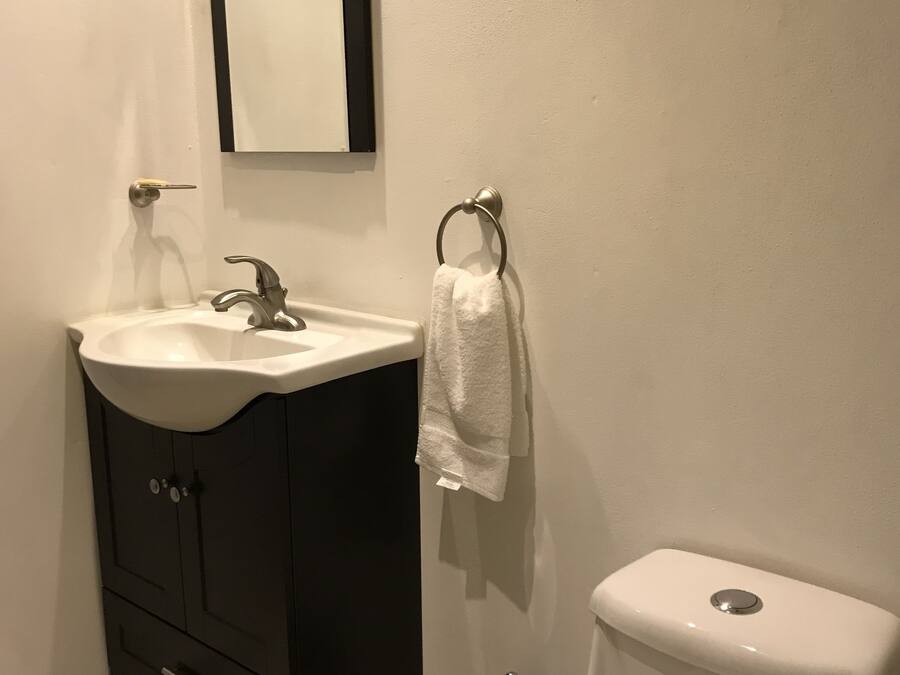 Une salle de bain avec un lavabo blanc, un meuble sombre, des toilettes et une serviette suspendue à un porte-serviette en forme d’anneau.