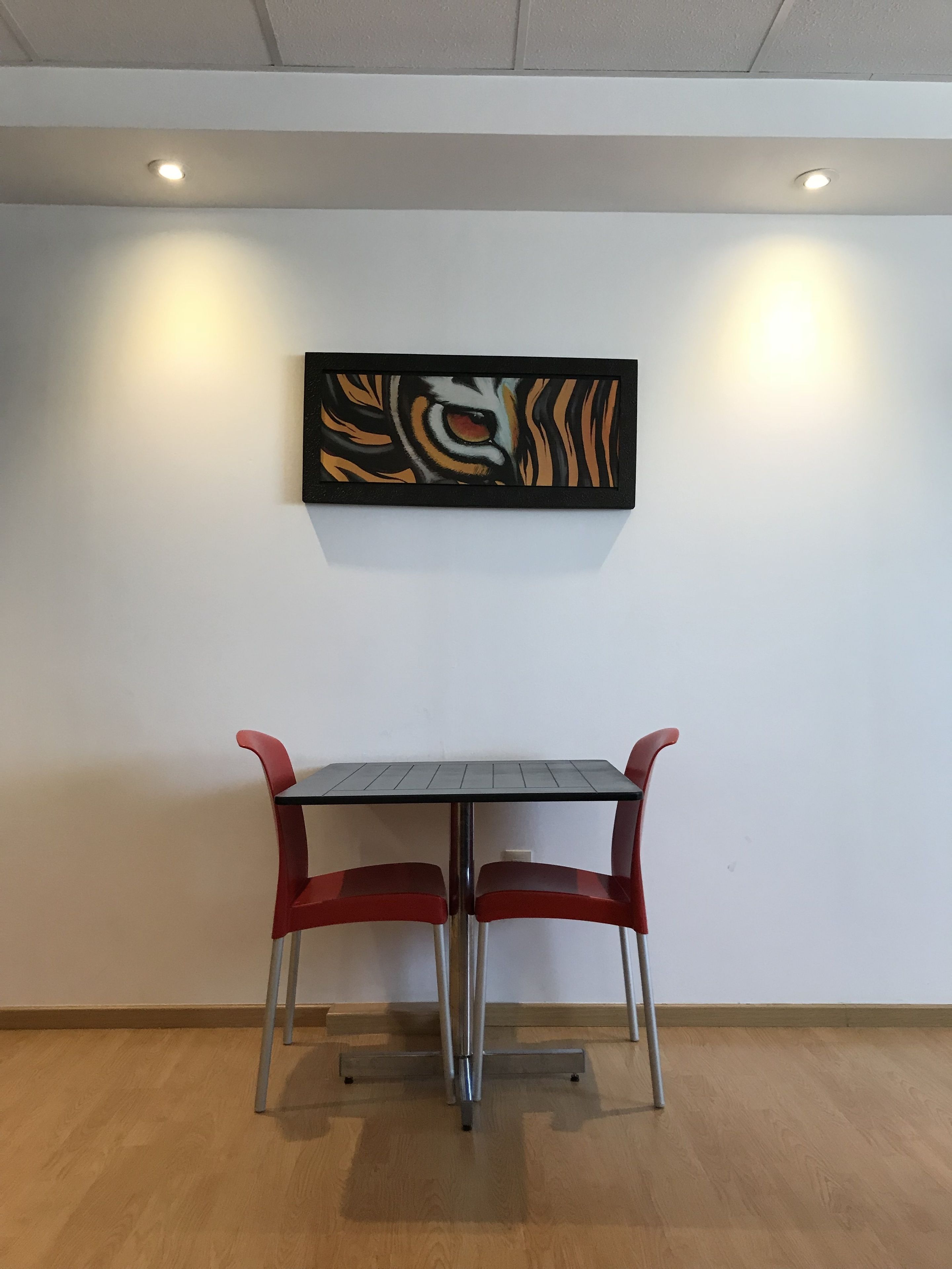 A dining area with a table and chairs, a ceiling with recessed lighting, and a wall-mounted artwork.