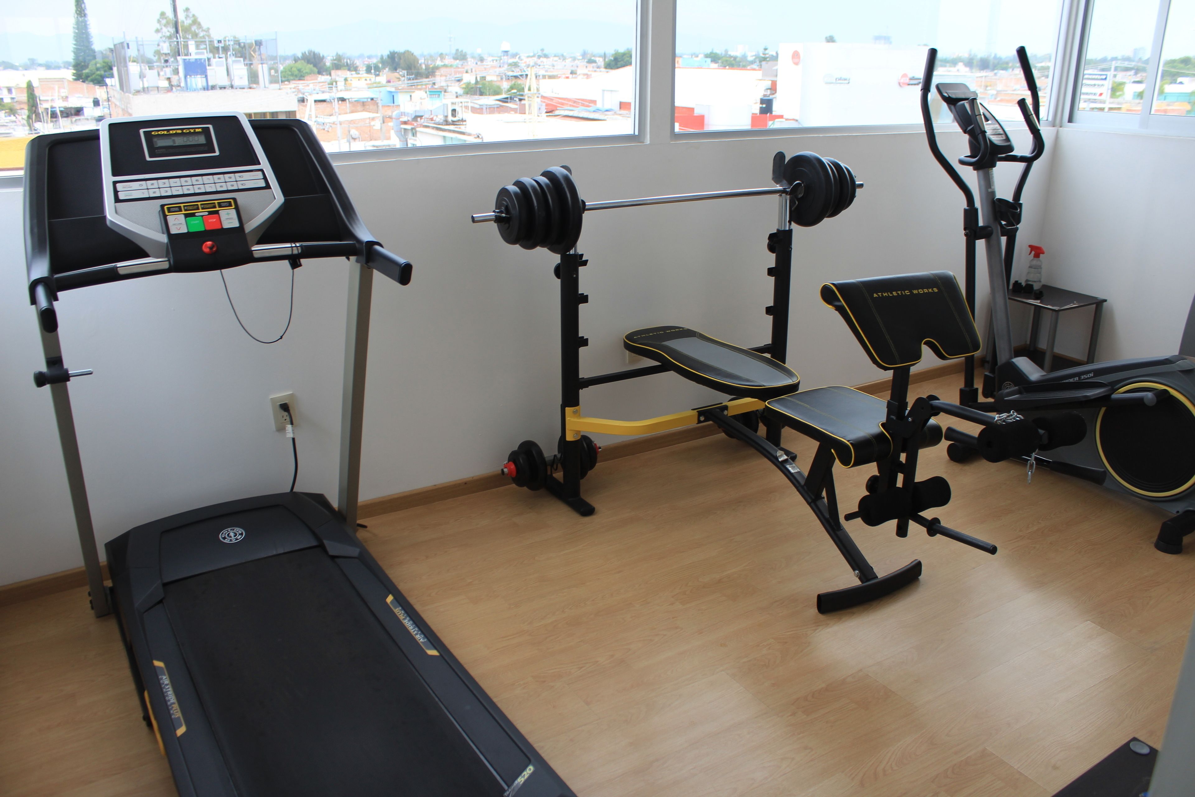 A gym with a treadmill, weight bench, and barbell rack.