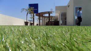 A grassy area with a modern building in the background, featuring a sign that reads "Nova Welcome". - My Home Suites (Celaya)