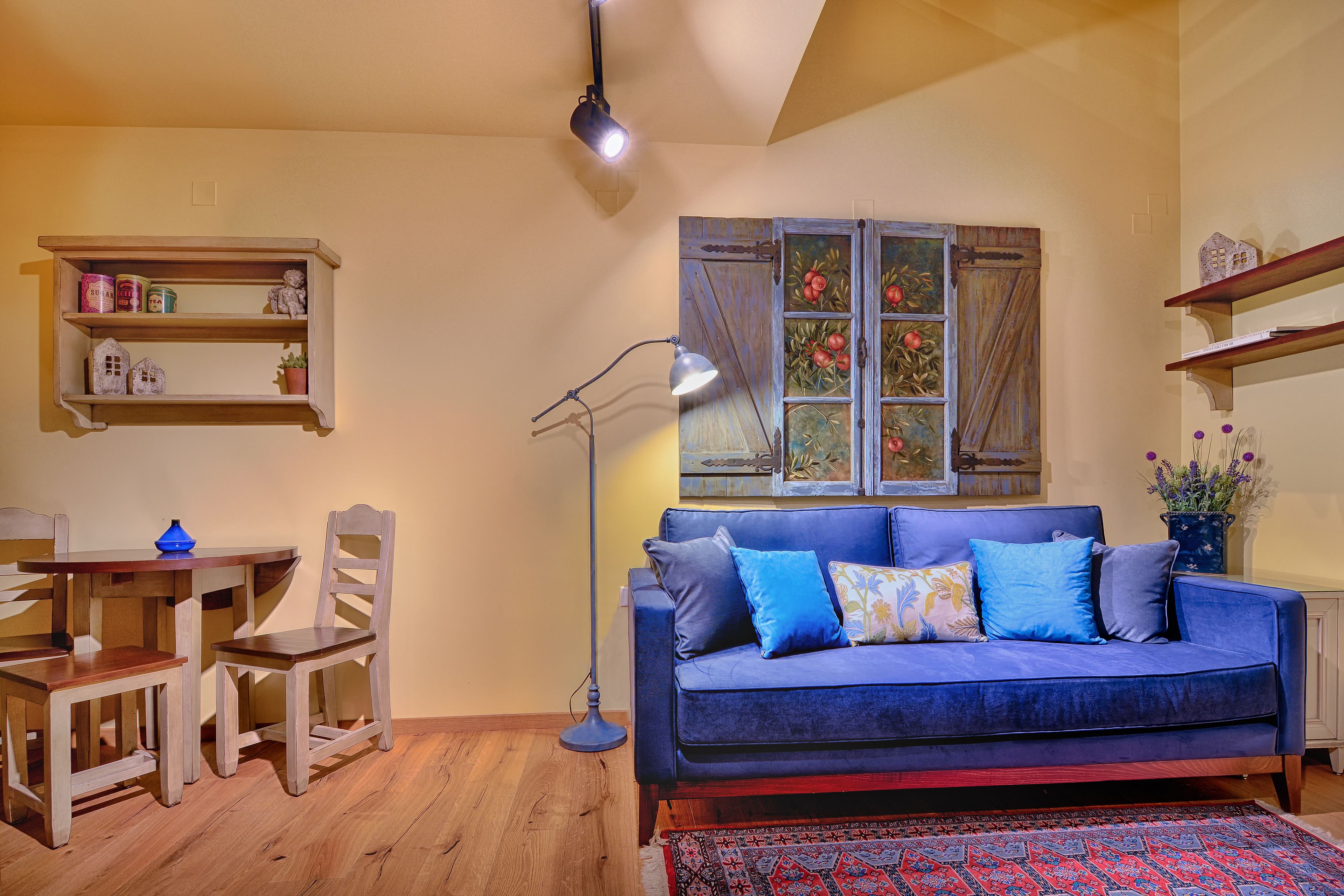 A living room with a blue sofa, wooden chairs, a small table, and a floor lamp.