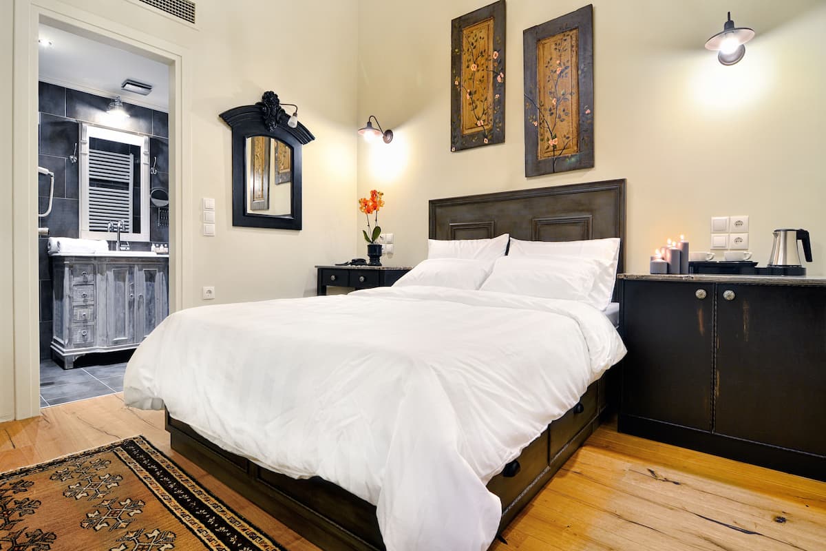 A bedroom with a large bed, a nightstand with a lamp, a dresser, and a mirror.
