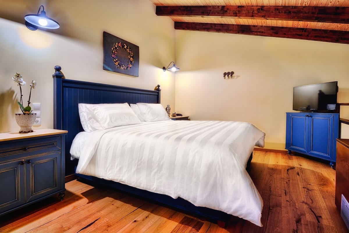 A bedroom with a bed, bedside tables, a TV, and a wall-mounted light fixture.