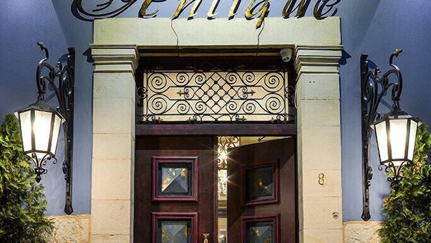 Der Eingang des Antique Hotels mit einer dunklen Holztür, je einer Pflanze in Töpfen auf jeder Seite und einem Schild darüber.