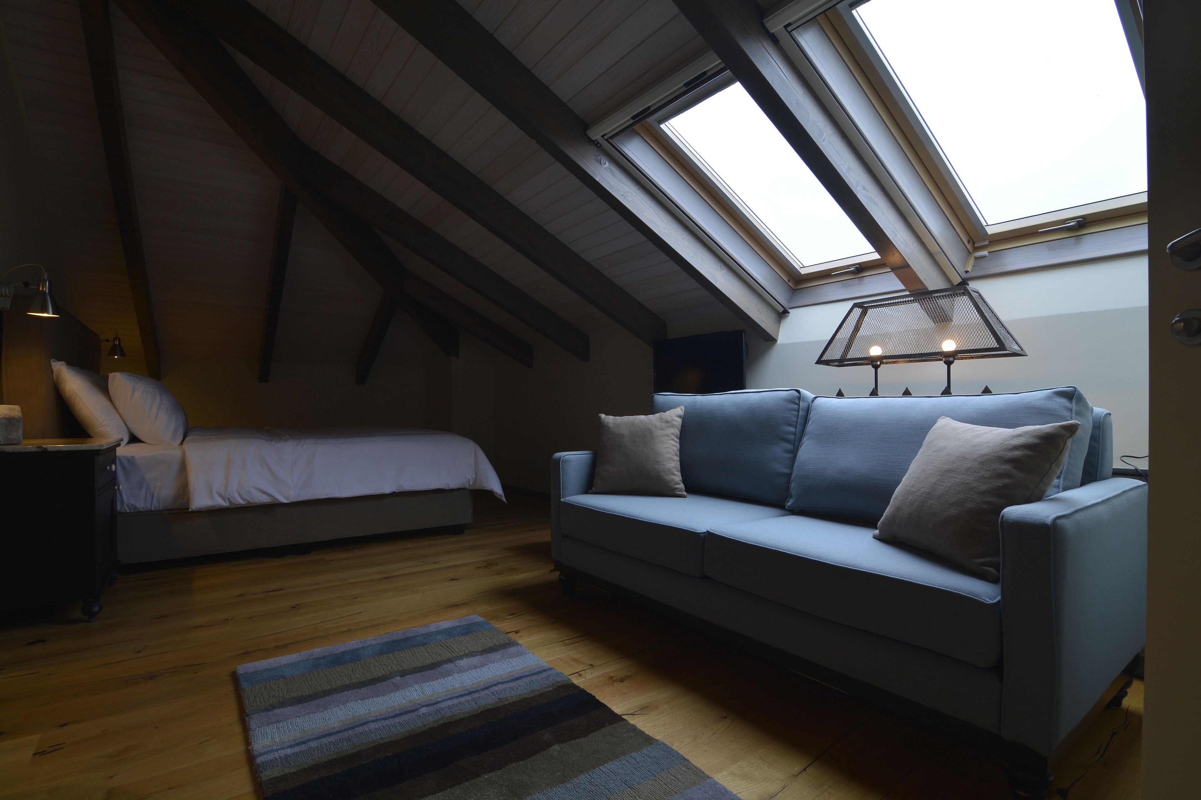 Un dormitorio tipo loft acogedor con techo inclinado, una cama, un sofá azul y un tragaluz.