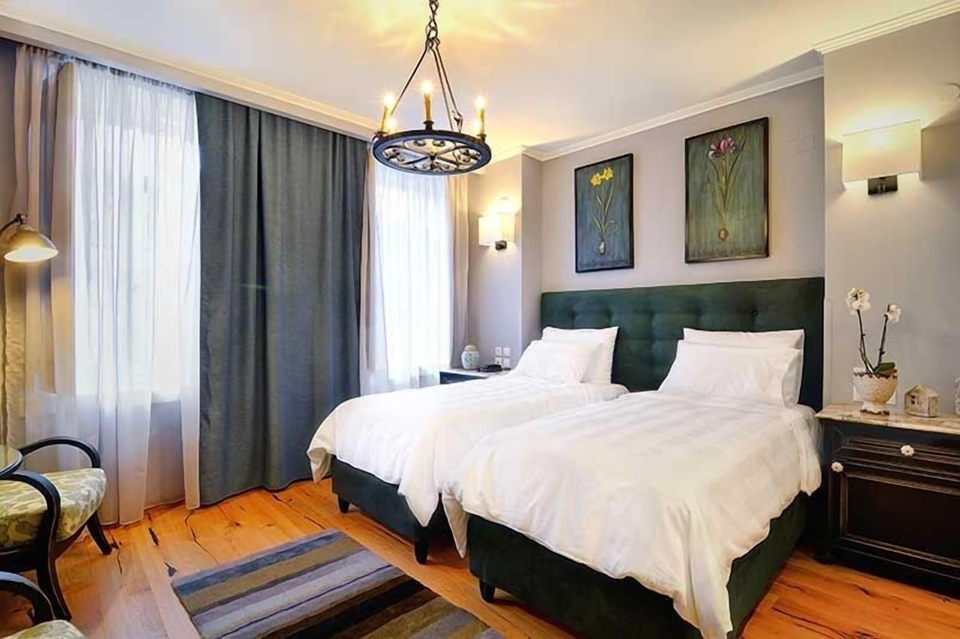 Ein Doppelbett mit grünem Kopfteil, ein Nachttisch mit Lampe und ein Fenster mit Vorhängen.