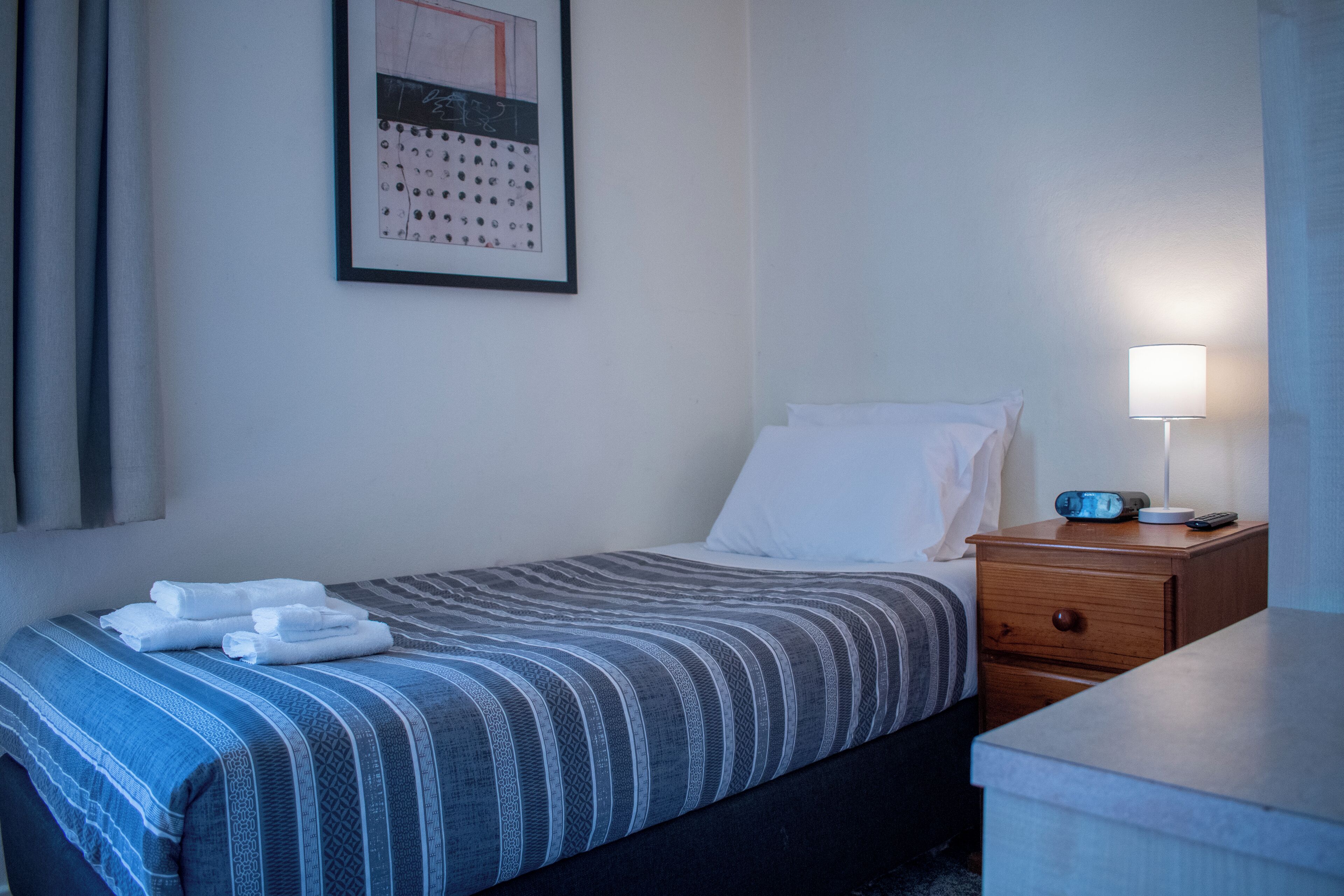 Une chambre d’hôtel avec un lit, une table de chevet, une lampe et un calendrier accroché au mur.