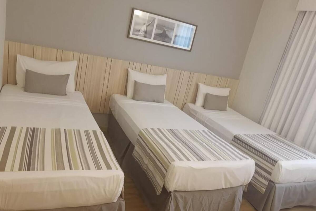 A hotel room with three single beds, each with a striped bedspread and a pillow.