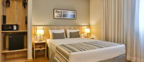 Una habitación de hotel con cama, lámparas de noche, un escritorio pequeño con lámpara, televisión y armario.