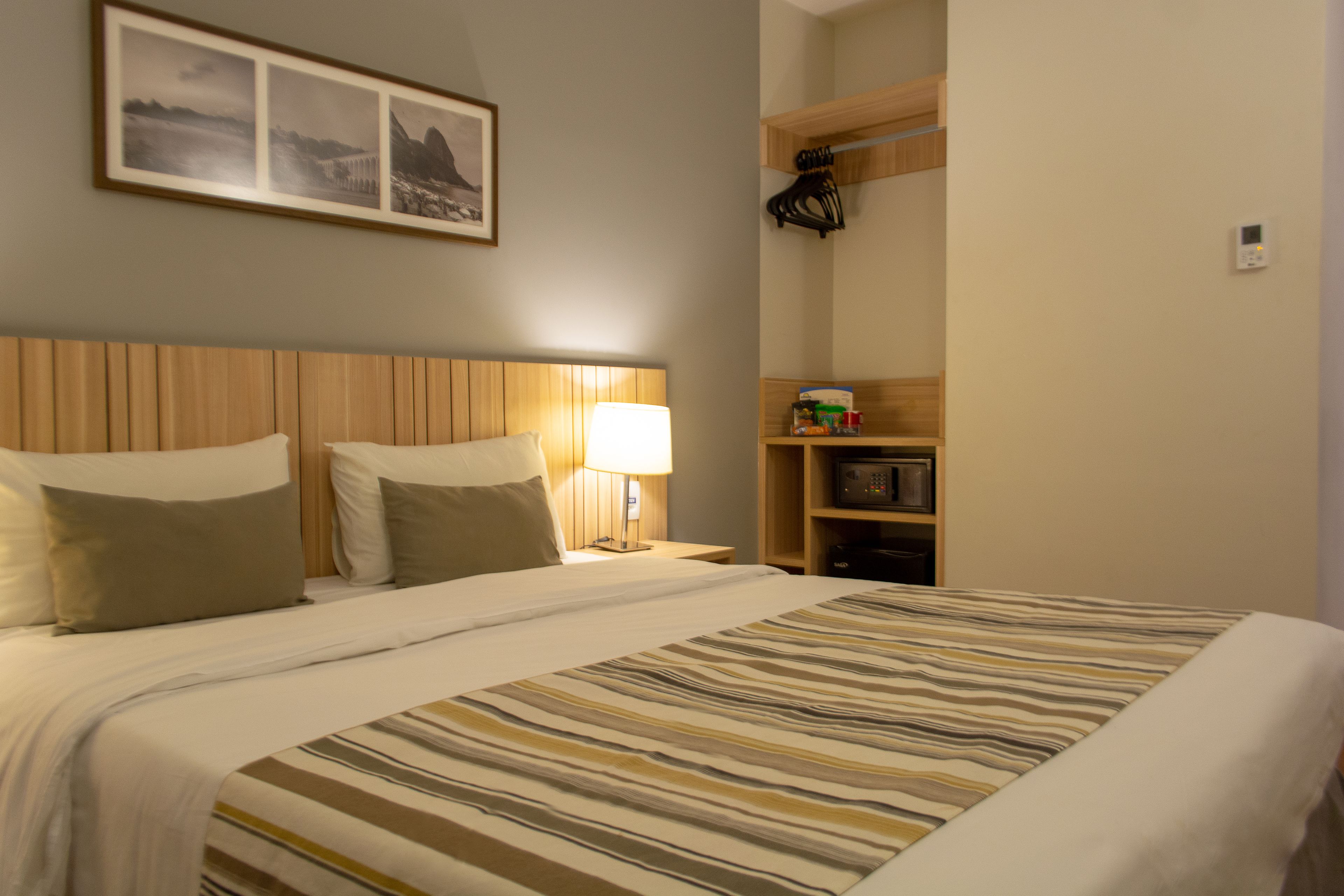 Une chambre d’hôtel comprenant un lit, une table de chevet, une lampe, une étagère avec des articles de toilette et un tableau encadré au mur.