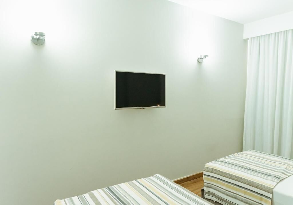 Una habitación con televisor de pantalla plana en la pared, una cama con ropa de cama a rayas y una ventana con cortinas.