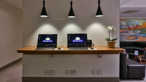 A reception desk with two laptops displaying 'Days Inn' on the screens, a potted plant, and a colorful mural on the wall. - Days Inn Rio de Janeiro, Lapa (Rio de Janeiro)