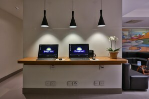 A reception desk with two laptops displaying 'Days Inn' on the screens, a potted plant, and a colorful mural on the wall.
